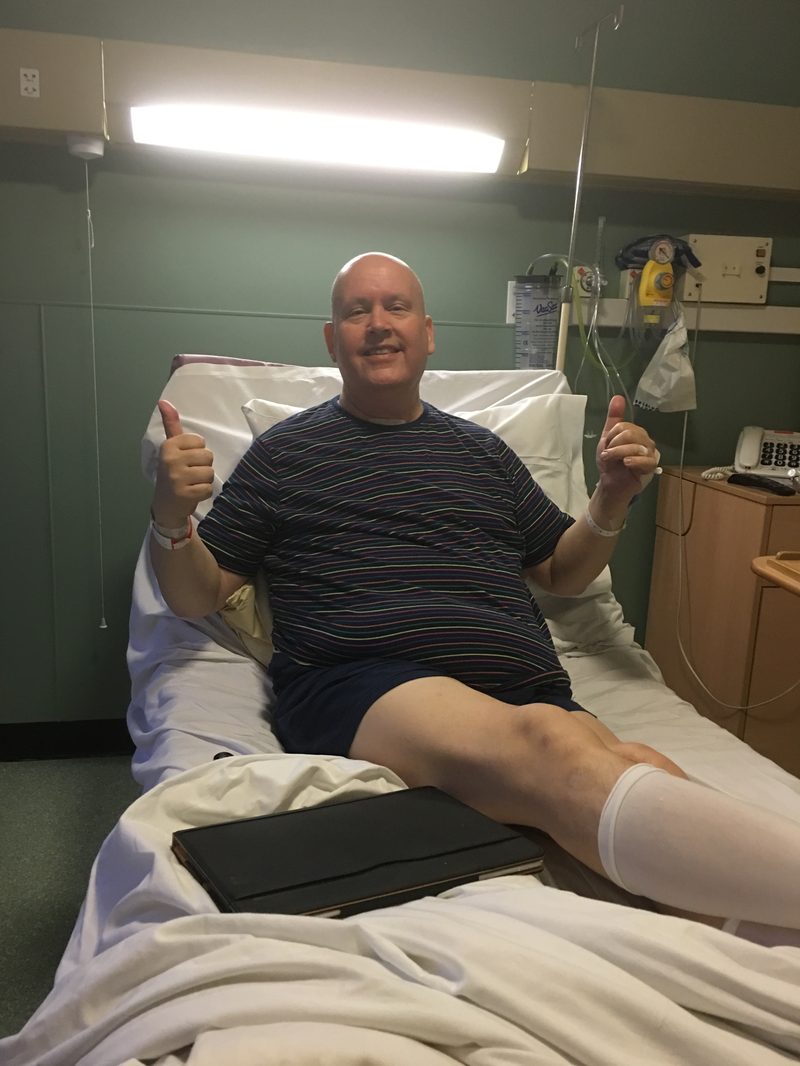 Dave in a hospital bed in October 2015, bald from chemotherapy, smiling and giving two thumbs up shortly after his mastectomy