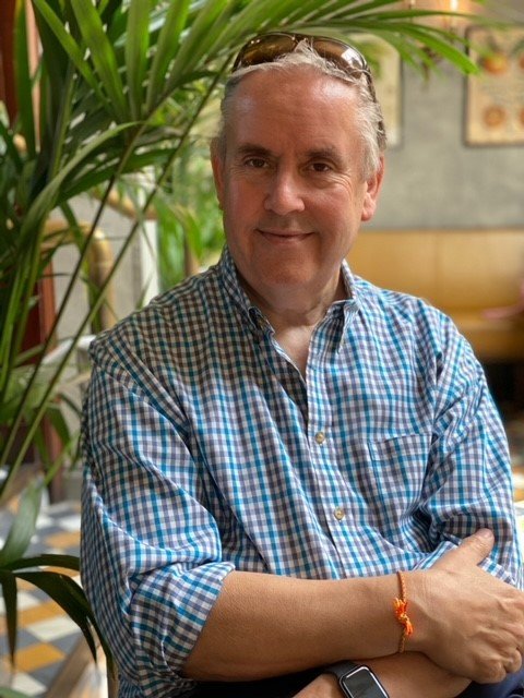 Dave Talbot, relaxed in a checked shirt with sunglasses on his head, arms folded, in a cafe